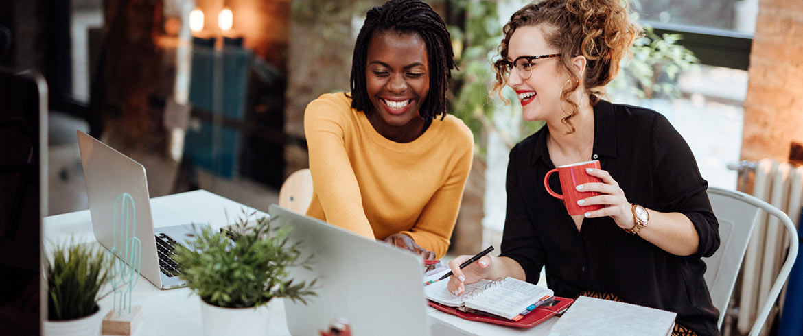 Two female coworkers at the office in front of laptops.