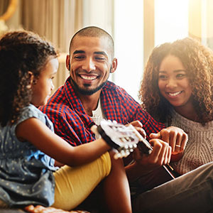 Young parents and daughter playing guitar at home.